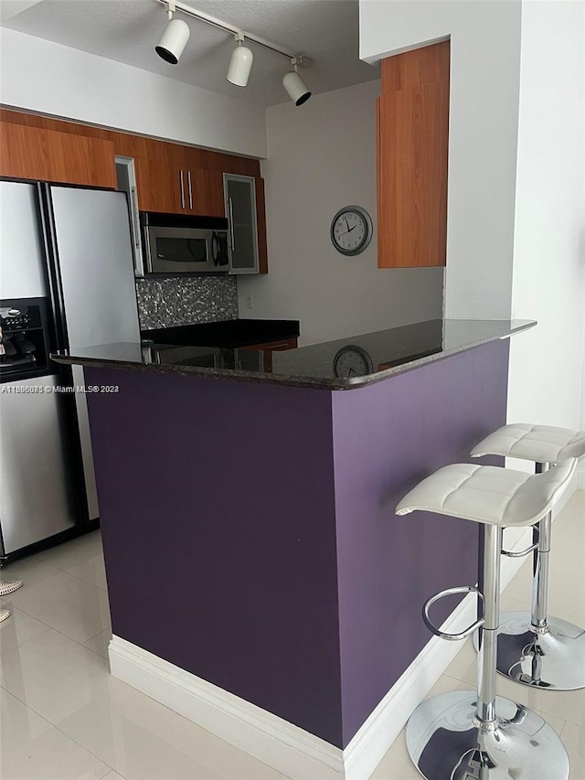 kitchen with kitchen peninsula, appliances with stainless steel finishes, tasteful backsplash, dark stone counters, and light tile patterned floors