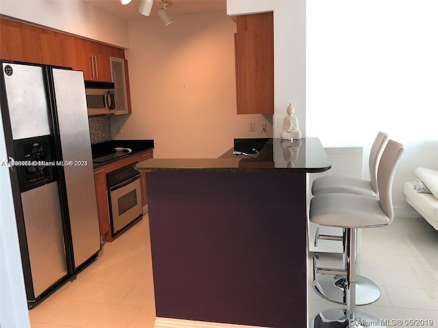 335 S Biscayne Blvd Unit 2202, Miami, FL 33131 - kitchen with stainless steel appliances, a peninsula, a breakfast bar area, brown cabinets, and light tile patterned floors