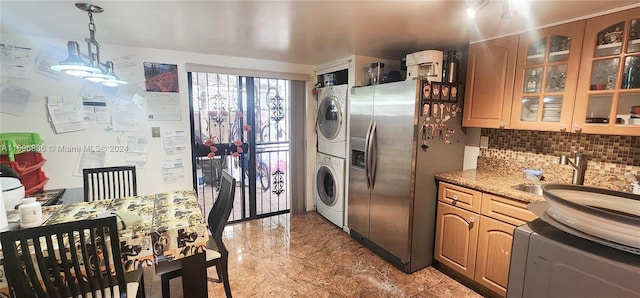 kitchen featuring light stone countertops, sink, stainless steel fridge, decorative light fixtures, and stacked washer and clothes dryer