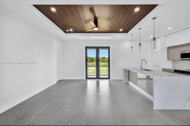 kitchen featuring white cabinetry, sink, a raised ceiling, light stone counters, and pendant lighting