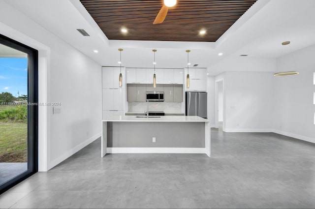 kitchen featuring pendant lighting, a raised ceiling, an island with sink, white cabinetry, and stainless steel appliances