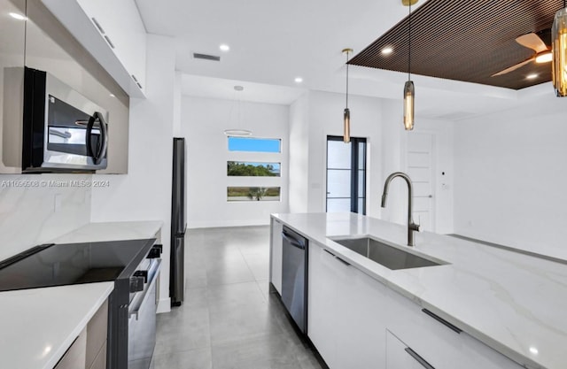 kitchen featuring pendant lighting, sink, light stone countertops, appliances with stainless steel finishes, and white cabinetry