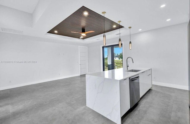 kitchen with white cabinetry, sink, hanging light fixtures, a raised ceiling, and an island with sink