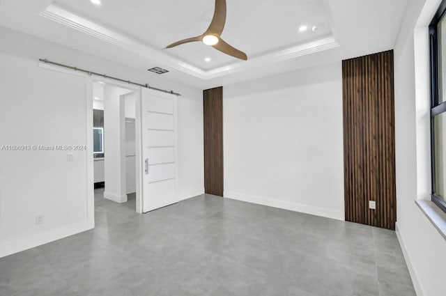 interior space with ceiling fan, a barn door, a raised ceiling, and concrete flooring