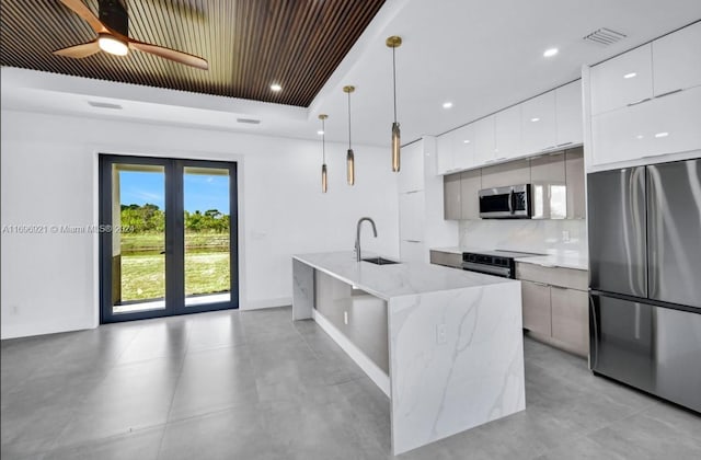 kitchen with backsplash, stainless steel appliances, a kitchen island with sink, white cabinets, and hanging light fixtures