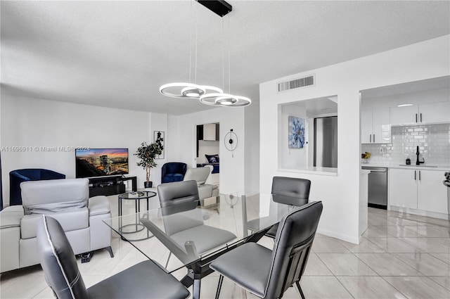 tiled dining space with sink, a textured ceiling, and a notable chandelier