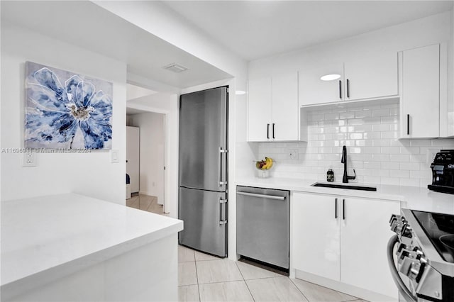 kitchen with decorative backsplash, appliances with stainless steel finishes, sink, light tile patterned floors, and white cabinetry