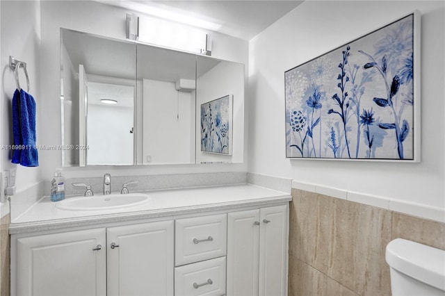 bathroom featuring vanity, toilet, and tile walls