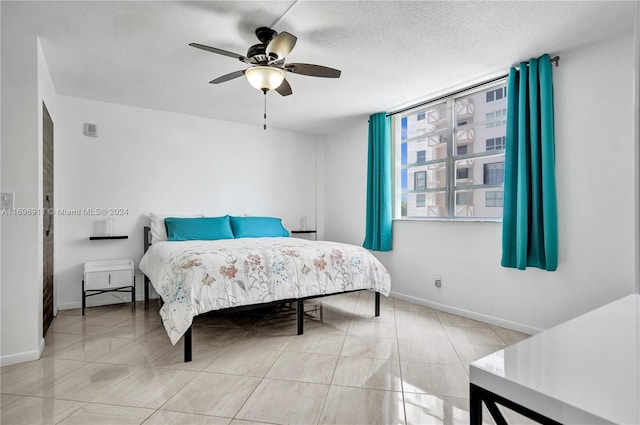 bedroom with ceiling fan, light tile patterned floors, and a textured ceiling