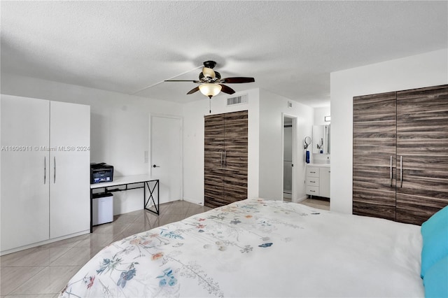 bedroom with ensuite bathroom, a textured ceiling, ceiling fan, light tile patterned floors, and a closet