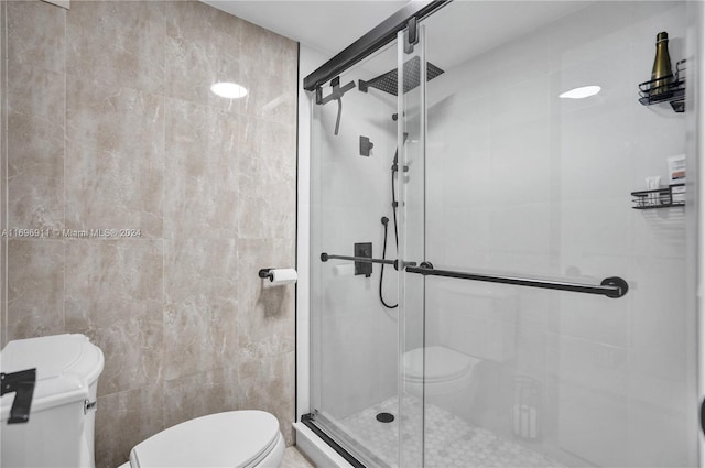 bathroom featuring a shower with door, tile walls, and toilet