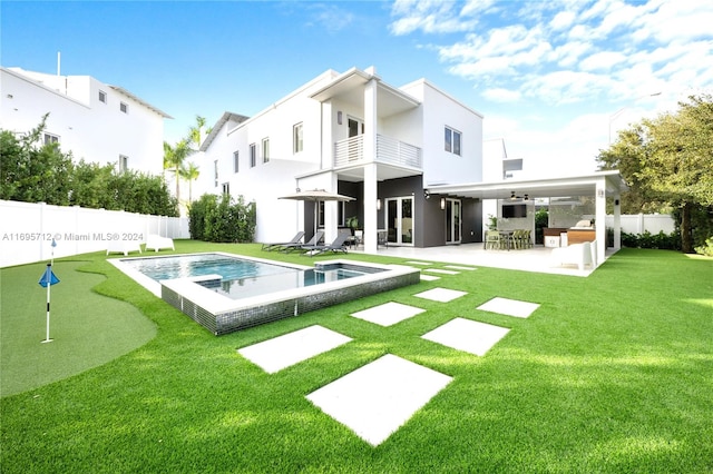 back of property with a balcony, ceiling fan, a patio area, a fenced in pool, and a lawn