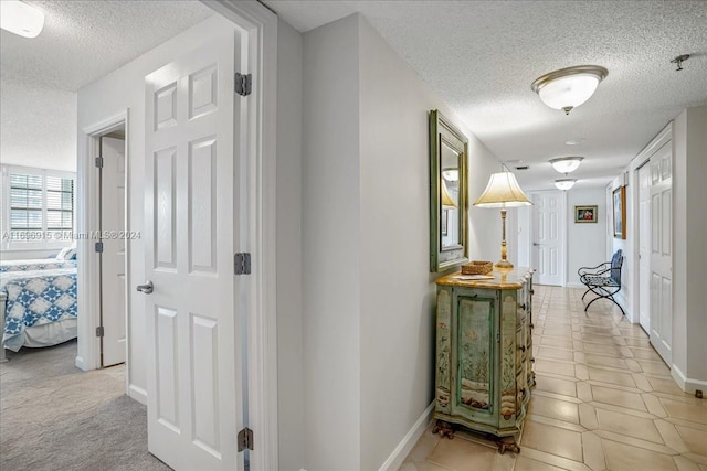 hallway featuring light colored carpet and a textured ceiling