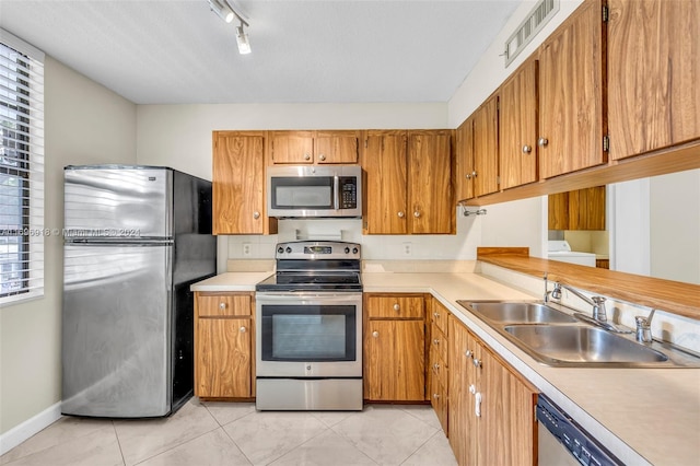 kitchen with sink, rail lighting, stainless steel appliances, washer / dryer, and light tile patterned floors