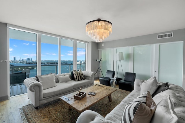 living room with hardwood / wood-style floors, a water view, an inviting chandelier, and floor to ceiling windows