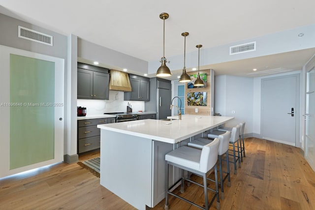 kitchen with a breakfast bar, backsplash, hanging light fixtures, light hardwood / wood-style flooring, and an island with sink