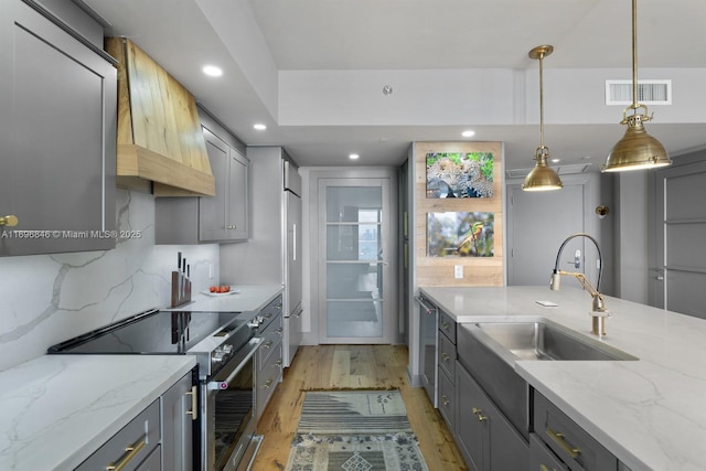 kitchen with gray cabinetry, high end appliances, sink, light hardwood / wood-style flooring, and hanging light fixtures