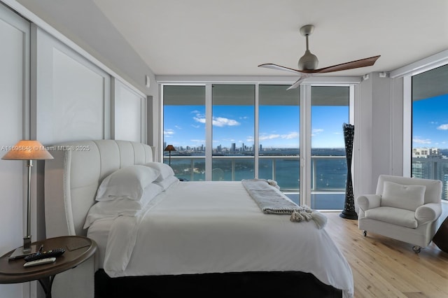 bedroom with ceiling fan, expansive windows, a water view, and light hardwood / wood-style floors