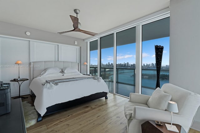 bedroom with expansive windows, access to outside, ceiling fan, hardwood / wood-style flooring, and a water view