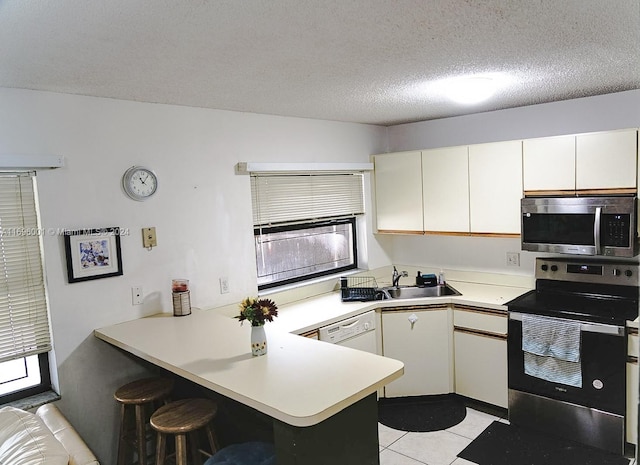 kitchen featuring kitchen peninsula, appliances with stainless steel finishes, a textured ceiling, sink, and a breakfast bar area