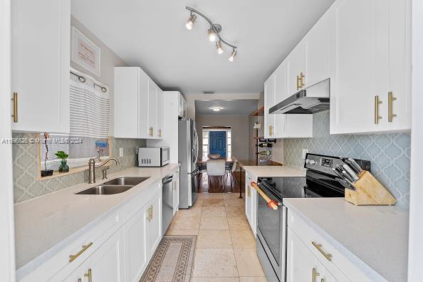 kitchen featuring appliances with stainless steel finishes, tasteful backsplash, sink, white cabinets, and light tile patterned flooring