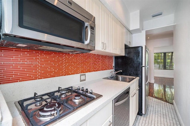 kitchen featuring stainless steel appliances, a sink, visible vents, white cabinetry, and backsplash