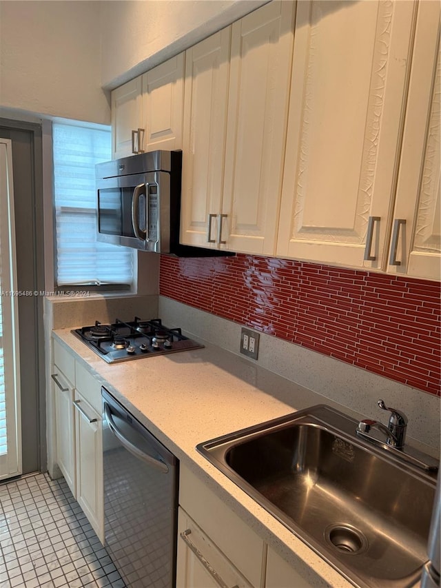 kitchen featuring sink, light tile patterned flooring, backsplash, white cabinets, and appliances with stainless steel finishes