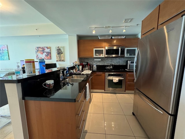 kitchen with decorative backsplash, kitchen peninsula, stainless steel appliances, sink, and light tile patterned floors