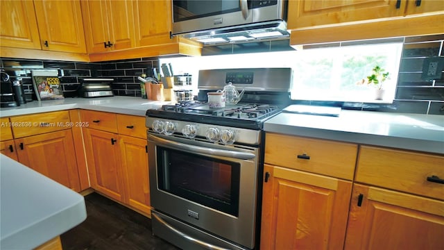 kitchen featuring brown cabinetry, stainless steel gas range oven, decorative backsplash, and light countertops