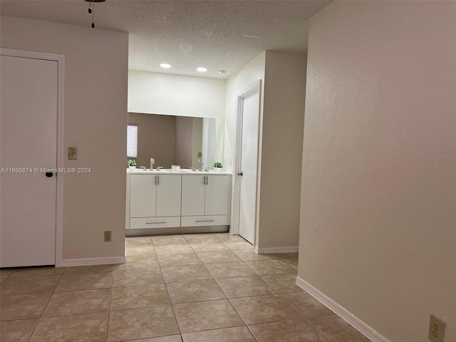 corridor with a textured ceiling, light tile patterned flooring, and sink