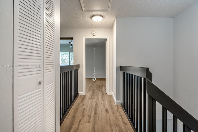 hall with light wood-type flooring and a textured ceiling