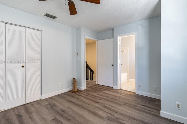 unfurnished bedroom with connected bathroom, ceiling fan, wood-type flooring, a textured ceiling, and a closet