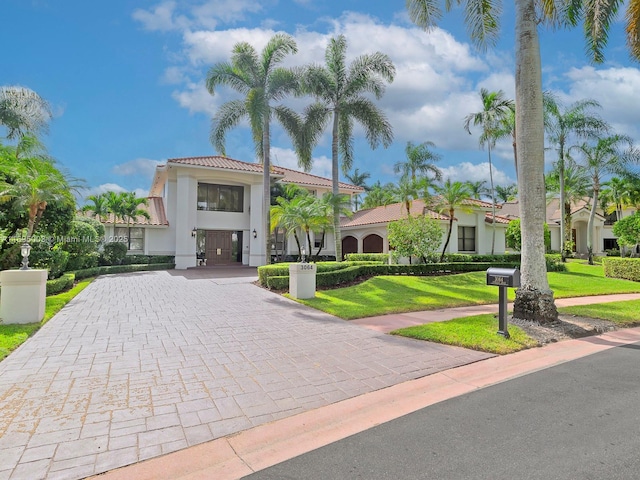 mediterranean / spanish-style house with stucco siding, a tiled roof, decorative driveway, and a front yard