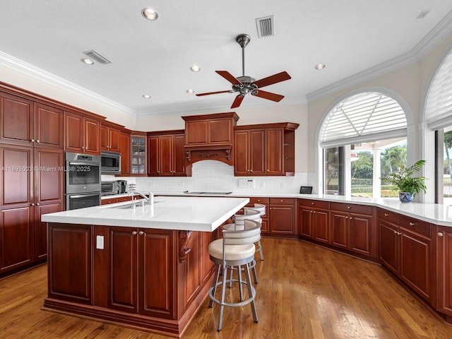 kitchen featuring backsplash, a center island with sink, sink, crown molding, and stainless steel appliances