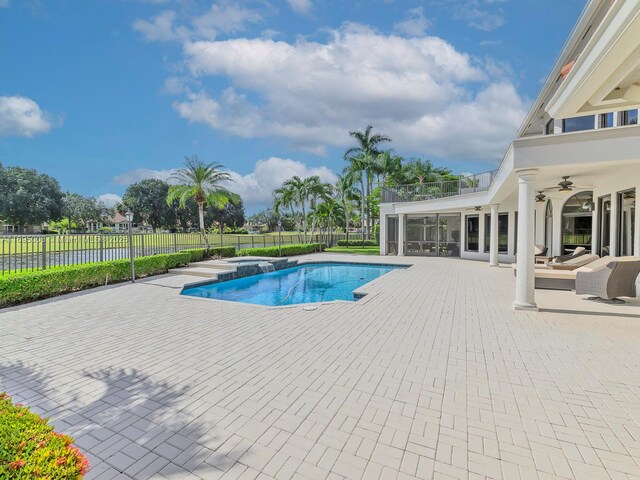 view of pool featuring an in ground hot tub, a water view, ceiling fan, and a patio area