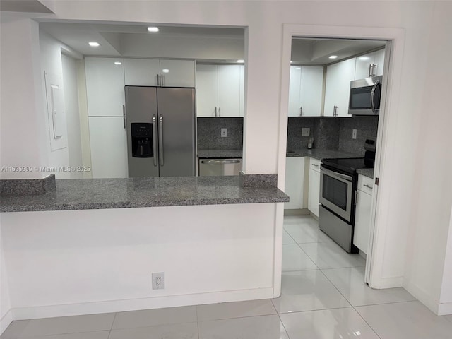 kitchen featuring dark stone countertops, decorative backsplash, light tile patterned flooring, white cabinetry, and appliances with stainless steel finishes