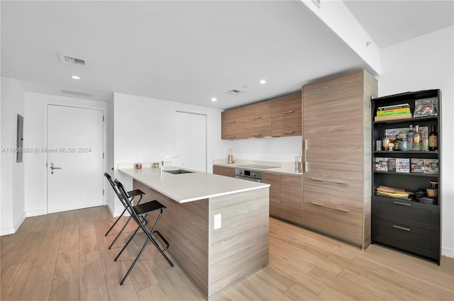 kitchen with a kitchen island with sink, black electric stovetop, sink, light hardwood / wood-style flooring, and a breakfast bar area