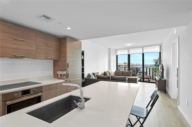 kitchen featuring a breakfast bar, stainless steel oven, floor to ceiling windows, black electric stovetop, and light wood-type flooring