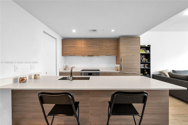 kitchen featuring a breakfast bar, light hardwood / wood-style floors, kitchen peninsula, and sink