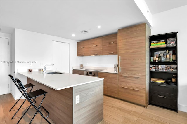 kitchen featuring kitchen peninsula, a kitchen breakfast bar, black electric cooktop, sink, and light hardwood / wood-style flooring