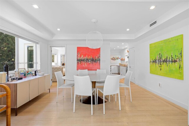 dining space featuring a raised ceiling and light hardwood / wood-style floors