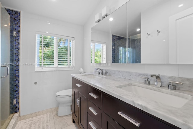 bathroom with tile patterned flooring, toilet, a shower with door, vanity, and tile walls