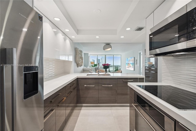 kitchen with sink, dark brown cabinets, a tray ceiling, stainless steel appliances, and white cabinets