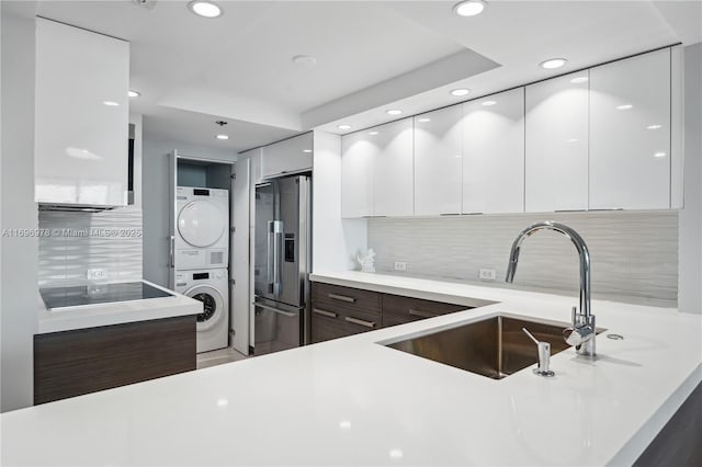 kitchen featuring sink, high end refrigerator, white cabinets, stacked washer and clothes dryer, and dark brown cabinetry