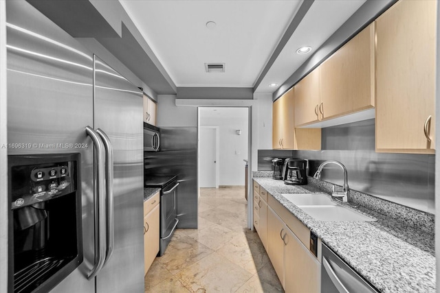 kitchen with light brown cabinets, sink, light stone countertops, and stainless steel appliances