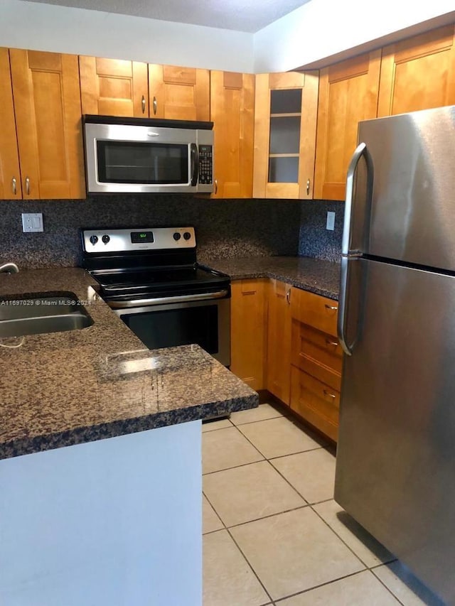 kitchen featuring backsplash, sink, stainless steel appliances, and dark stone counters