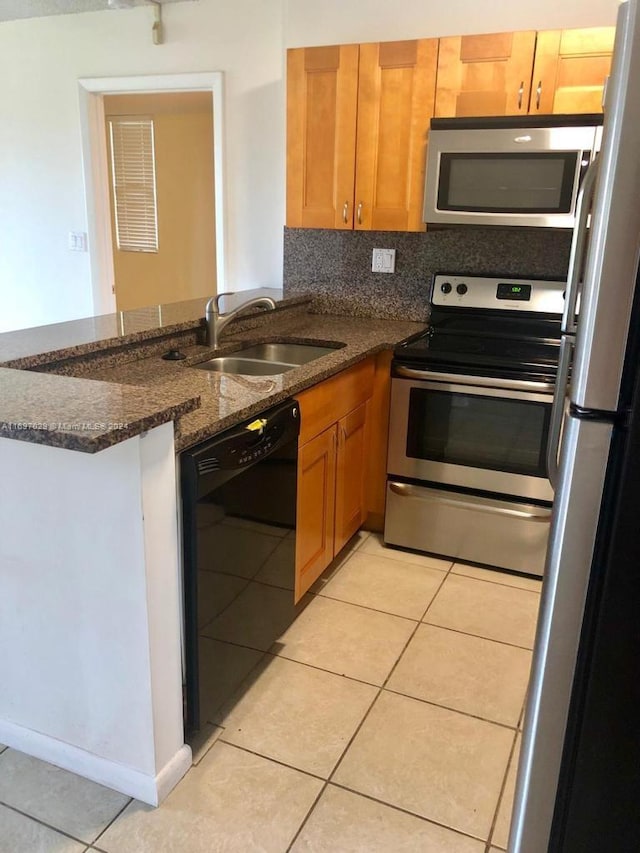 kitchen featuring sink, backsplash, dark stone countertops, light tile patterned flooring, and appliances with stainless steel finishes