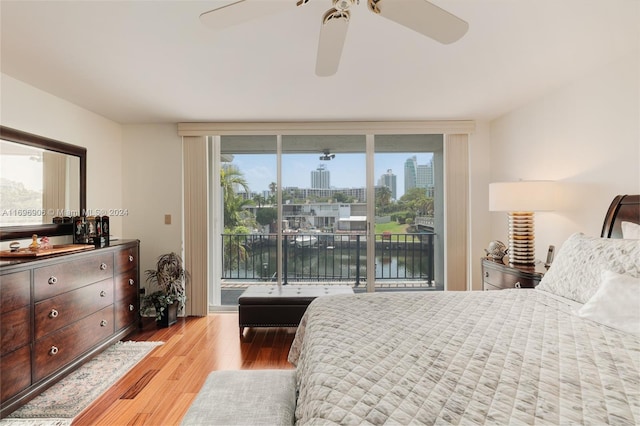 bedroom featuring access to exterior, light hardwood / wood-style floors, ceiling fan, and a water view