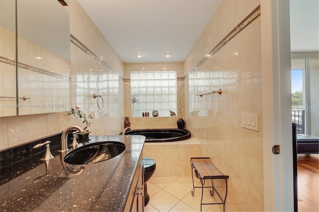 bathroom with vanity, wood-type flooring, tile walls, and tiled bath