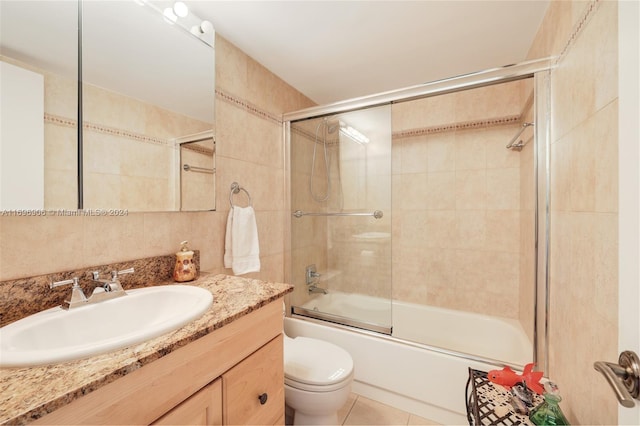 full bathroom with tile patterned flooring, enclosed tub / shower combo, toilet, vanity, and tile walls